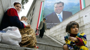 A mother and her children beg on a stairway, beneath a building with a huge sign of President Emomali Rakhmon. AFP