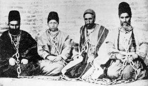 A Bahá’í father and son (at left) in chains after being arrested with fellow Bahá’ís, in a photograph taken around 1896. Both were subsequently executed.